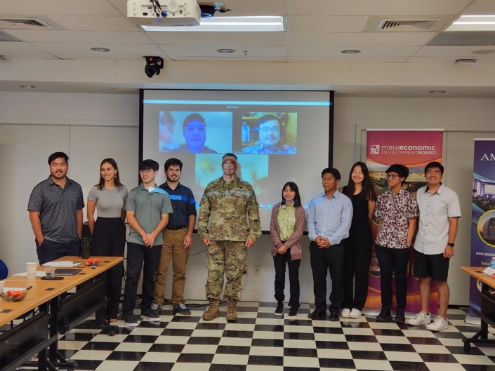 Participants and leaders pose in front of a video screen